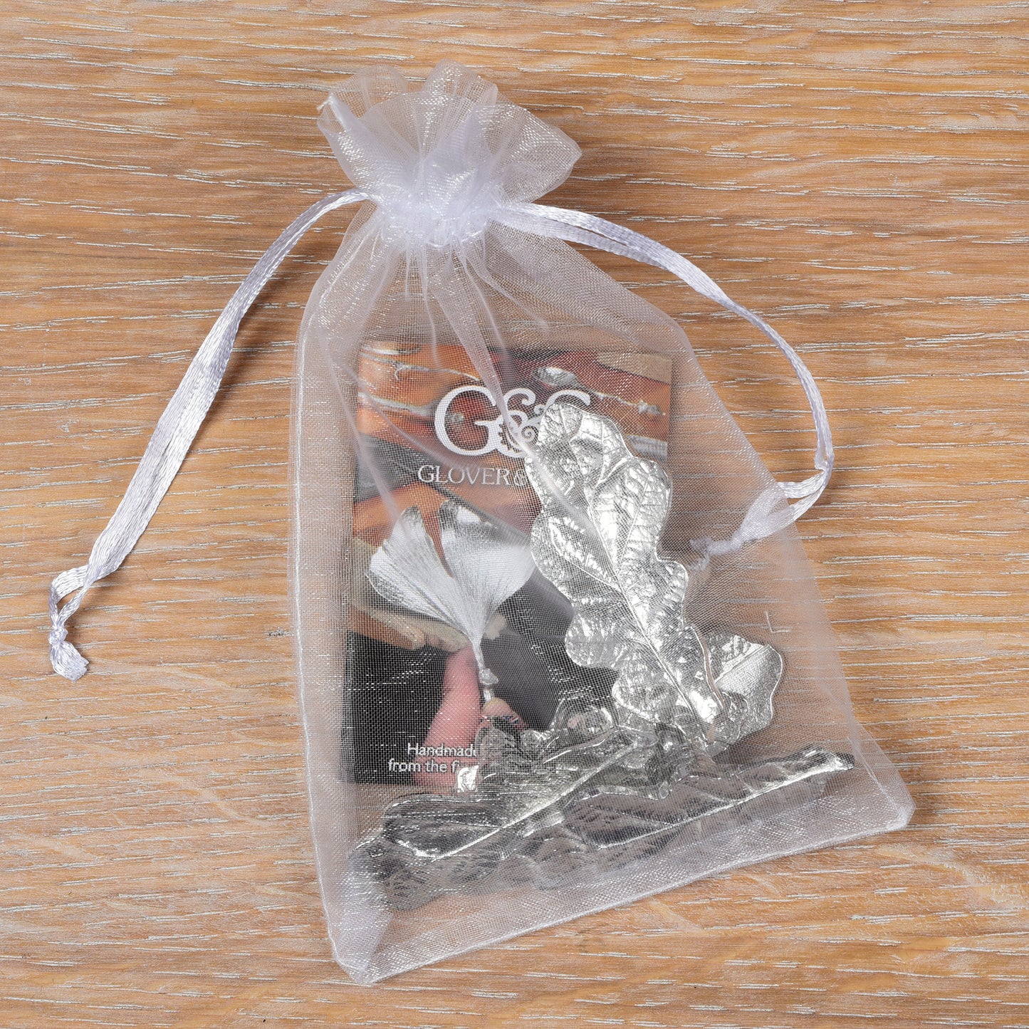 A set of four silver-colored pewter oak leaf place card holders in their packaging.