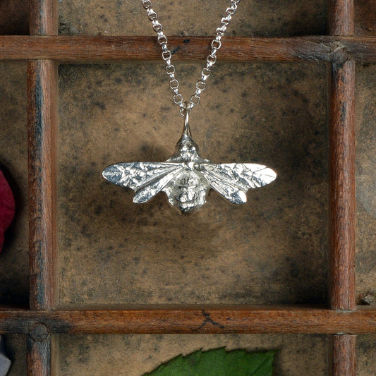 A silver-colored pewter honey bee pendant necklace with delicately detailed wings, displayed on a rustic wooden background.