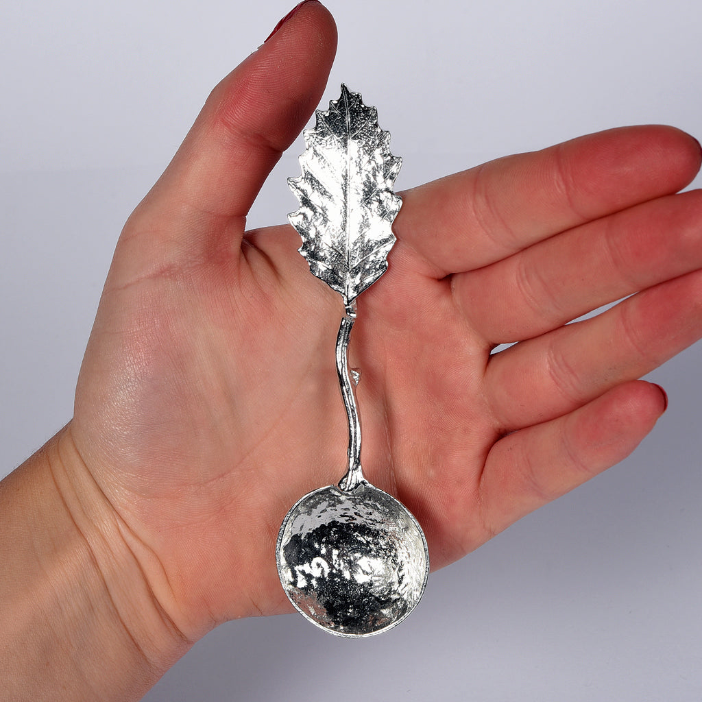 A small pewter sugar spoon with a detailed chestnut leaf on the end of a twig handle, handmade in the UK