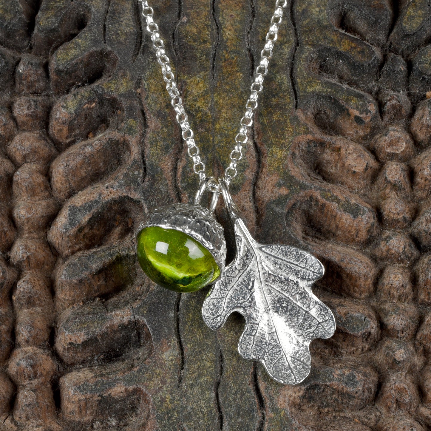 A peridot stone in a pewter acorn cup with an oak leaf on a Sterling silver chain. Necklace gift on a wooden textured background