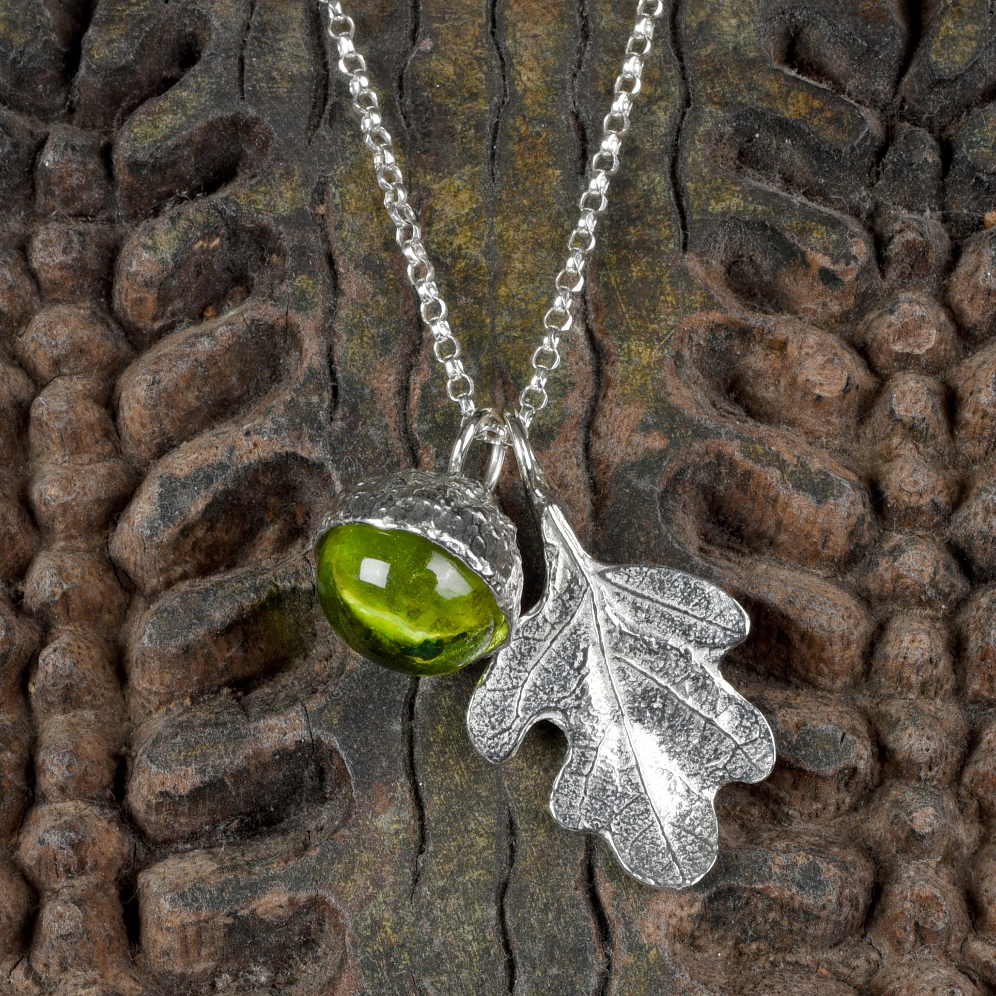 A peridot stone in a pewter acorn cup with an oak leaf on a Sterling silver chain. Necklace gift on a wooden textured background