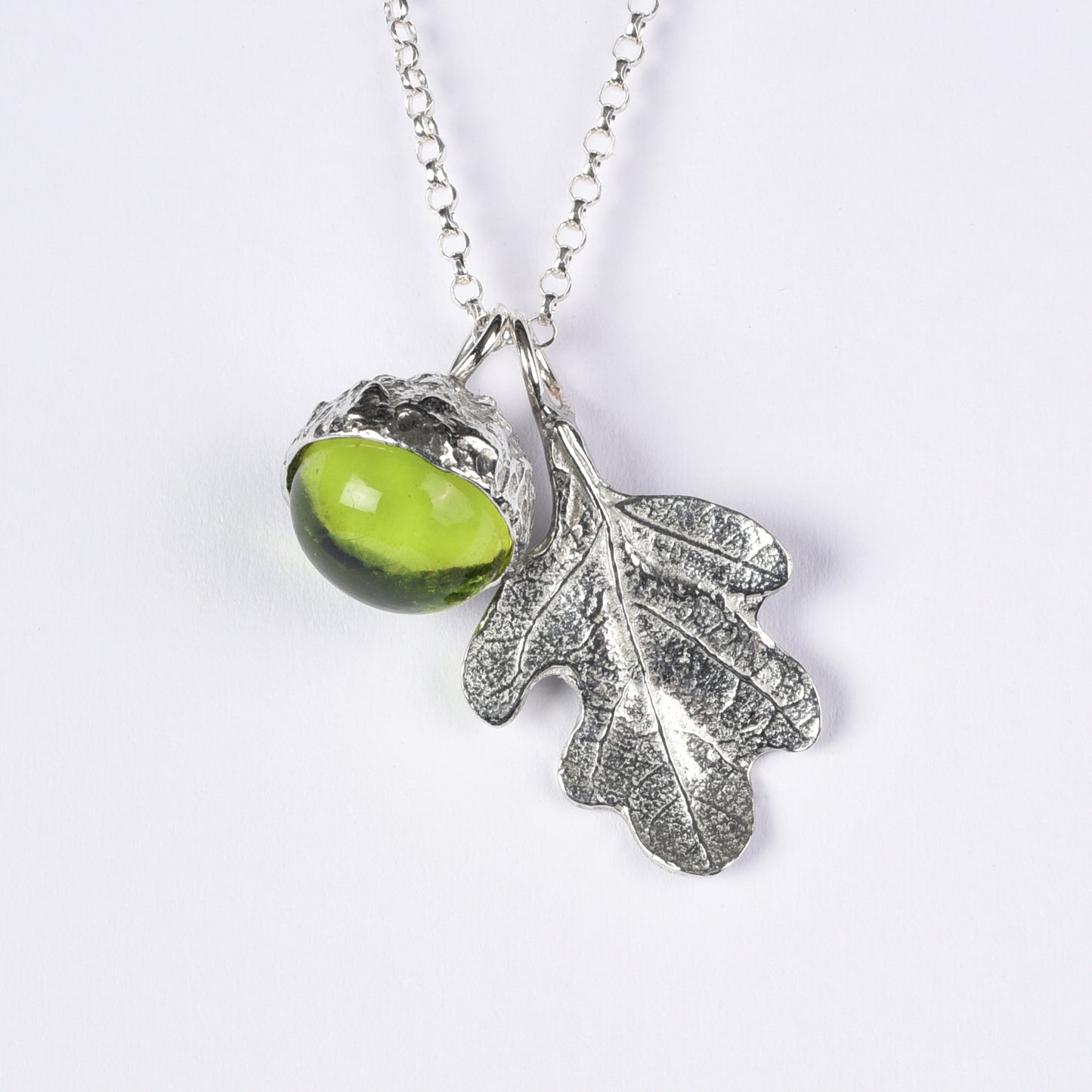 A peridot stone in a pewter acorn cup with an oak leaf on a Sterling silver chain. Necklace gift on a white background