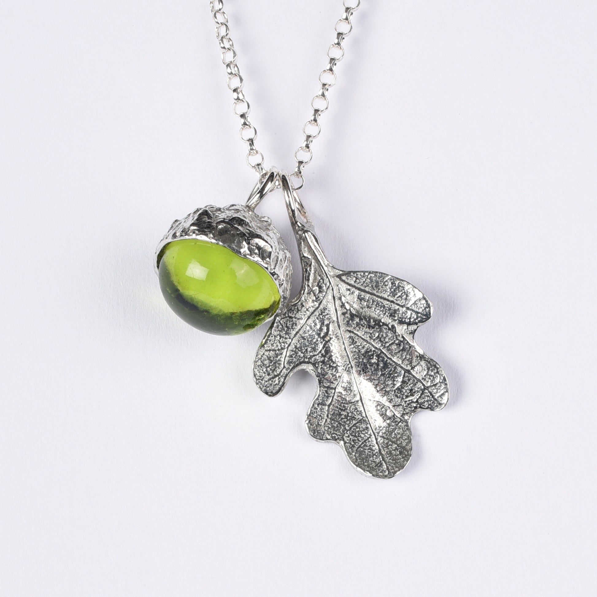 A peridot stone in a pewter acorn cup with an oak leaf on a Sterling silver chain. Necklace gift on a white background