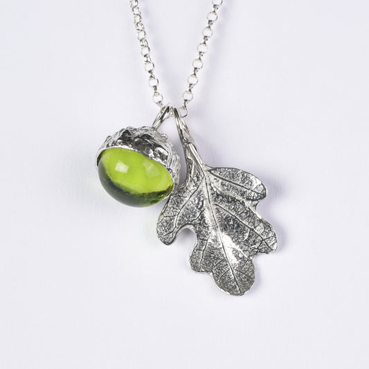 A peridot stone in a pewter acorn cup with an oak leaf on a Sterling silver chain. Necklace gift on a white background