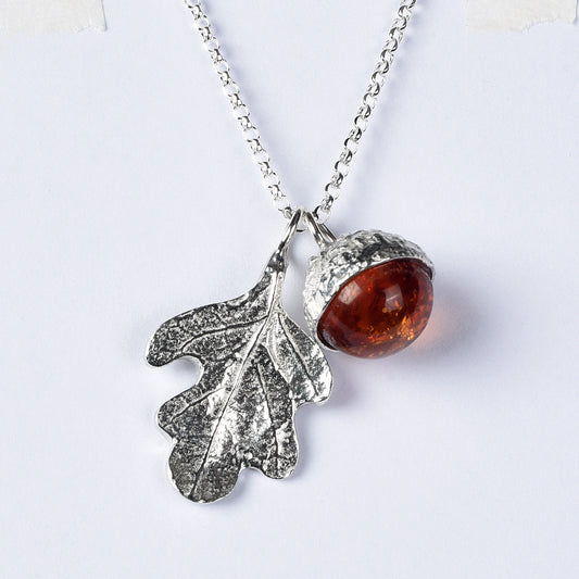 A delicate and detailed pewter oak leaf and amber acorn necklace on an 18" Sterling silver chain. A real amber stone in an acorn cup. Shown against a white background.