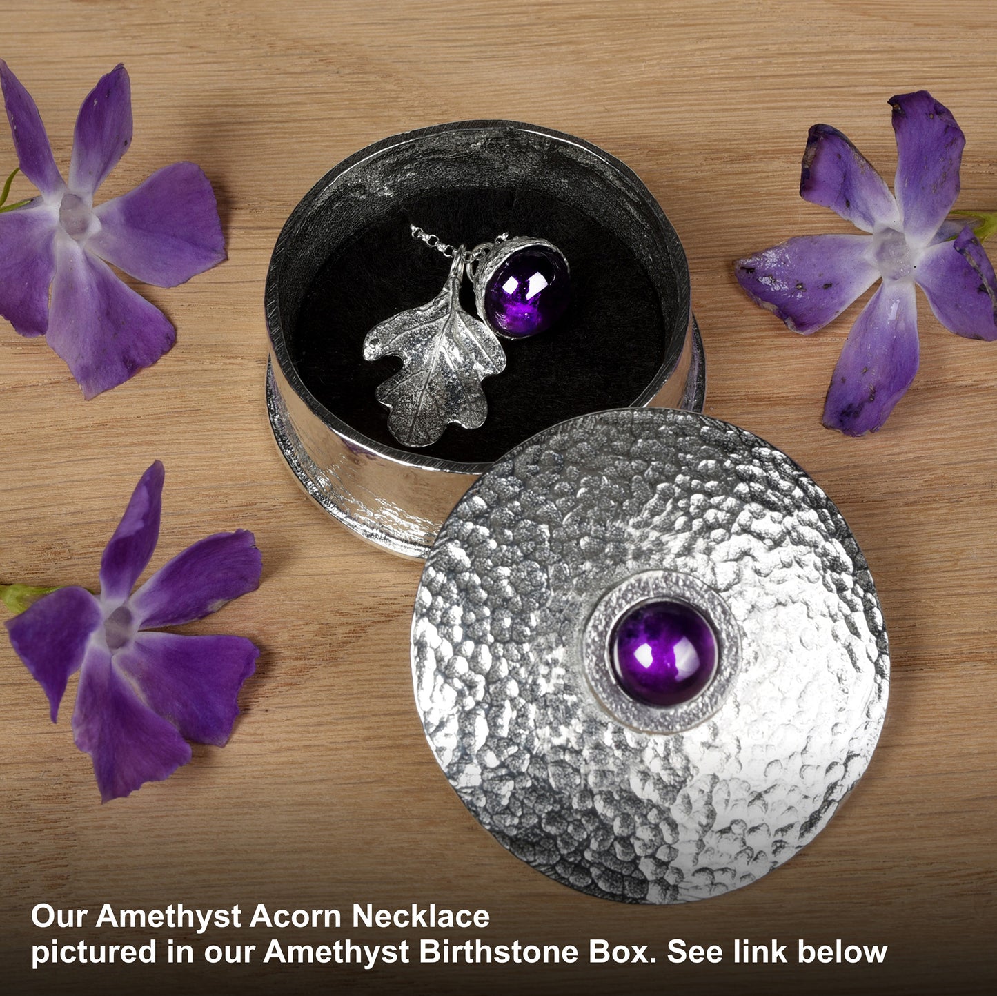 Amethyst Acorn Necklace in an Amethyst Birthstone Box with purple flowers on a wooden surface