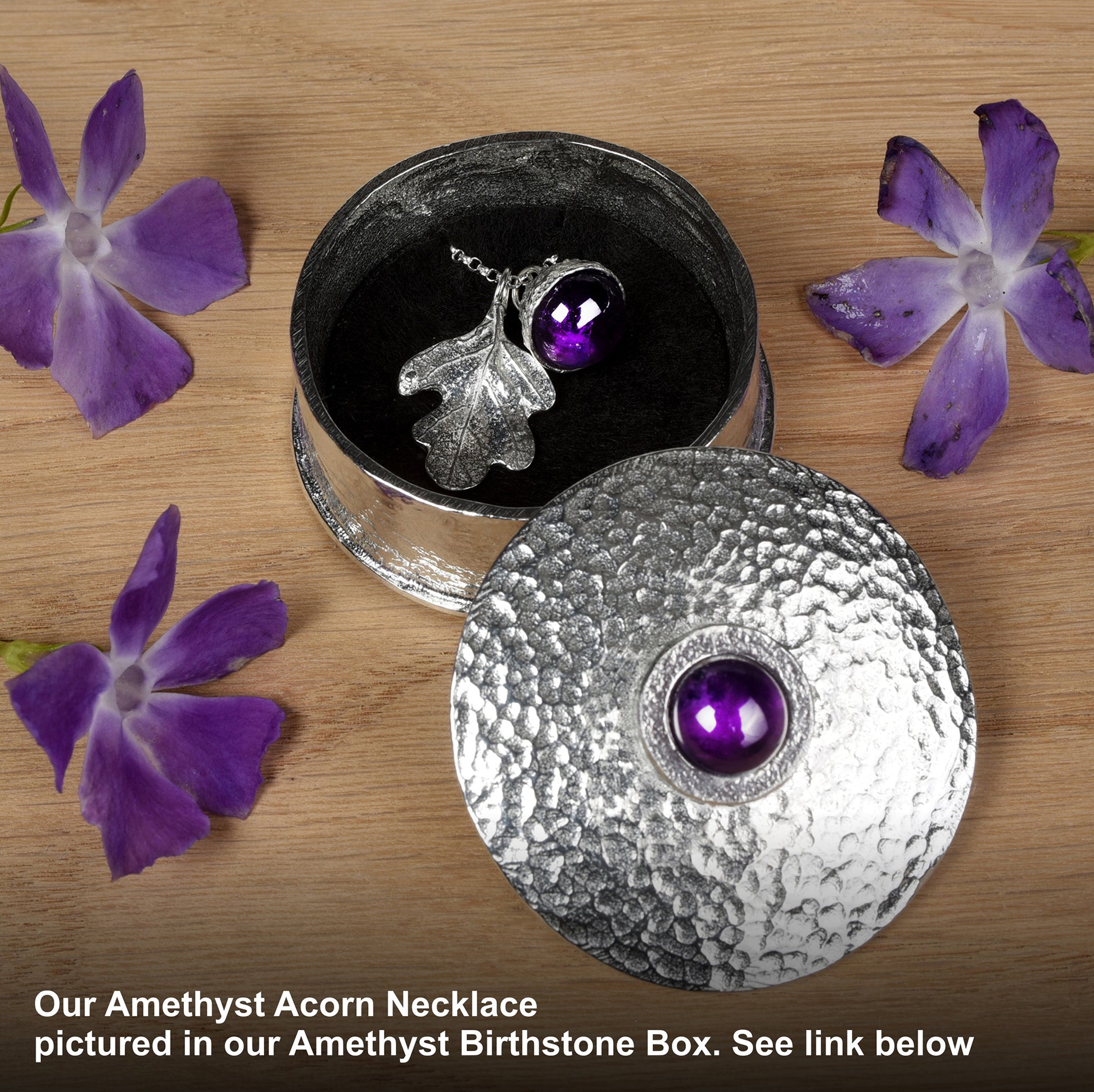 Amethyst Acorn Necklace in an Amethyst Birthstone Box with purple flowers on a wooden surface