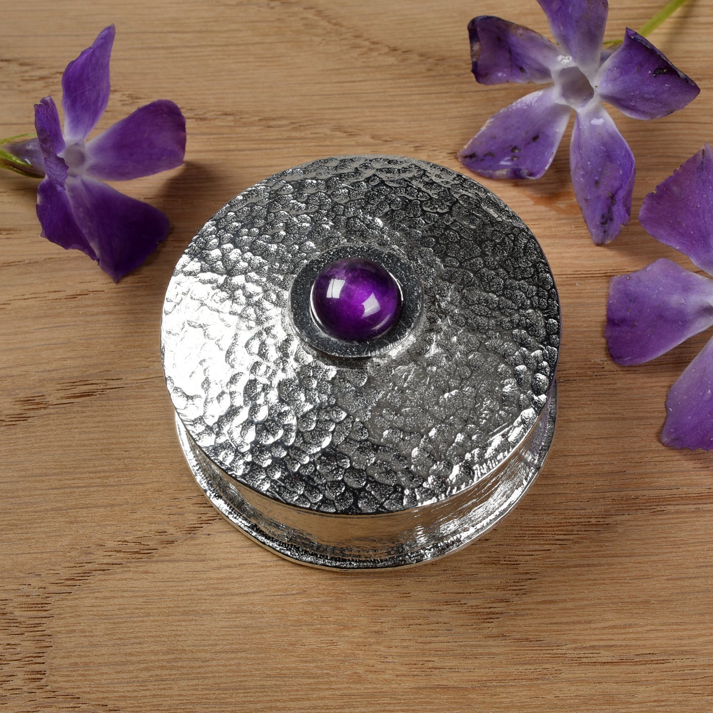 A simple textured pewter trinket box with a 10mm amethyst set into the centre of the lid. Amethyst is the birthstone for February.