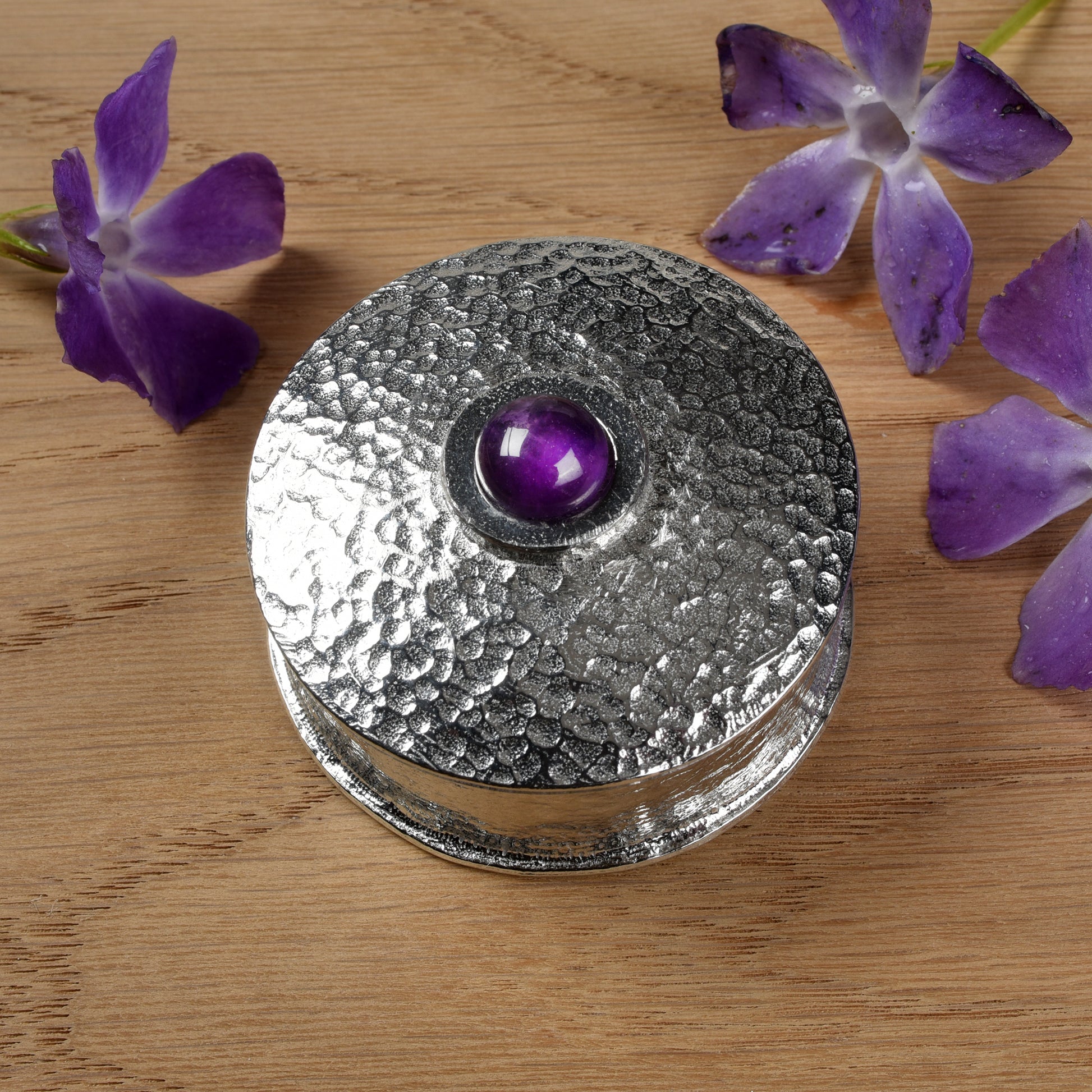 A simple textured pewter trinket box with a 10mm amethyst set into the centre of the lid. Amethyst is the birthstone for February.