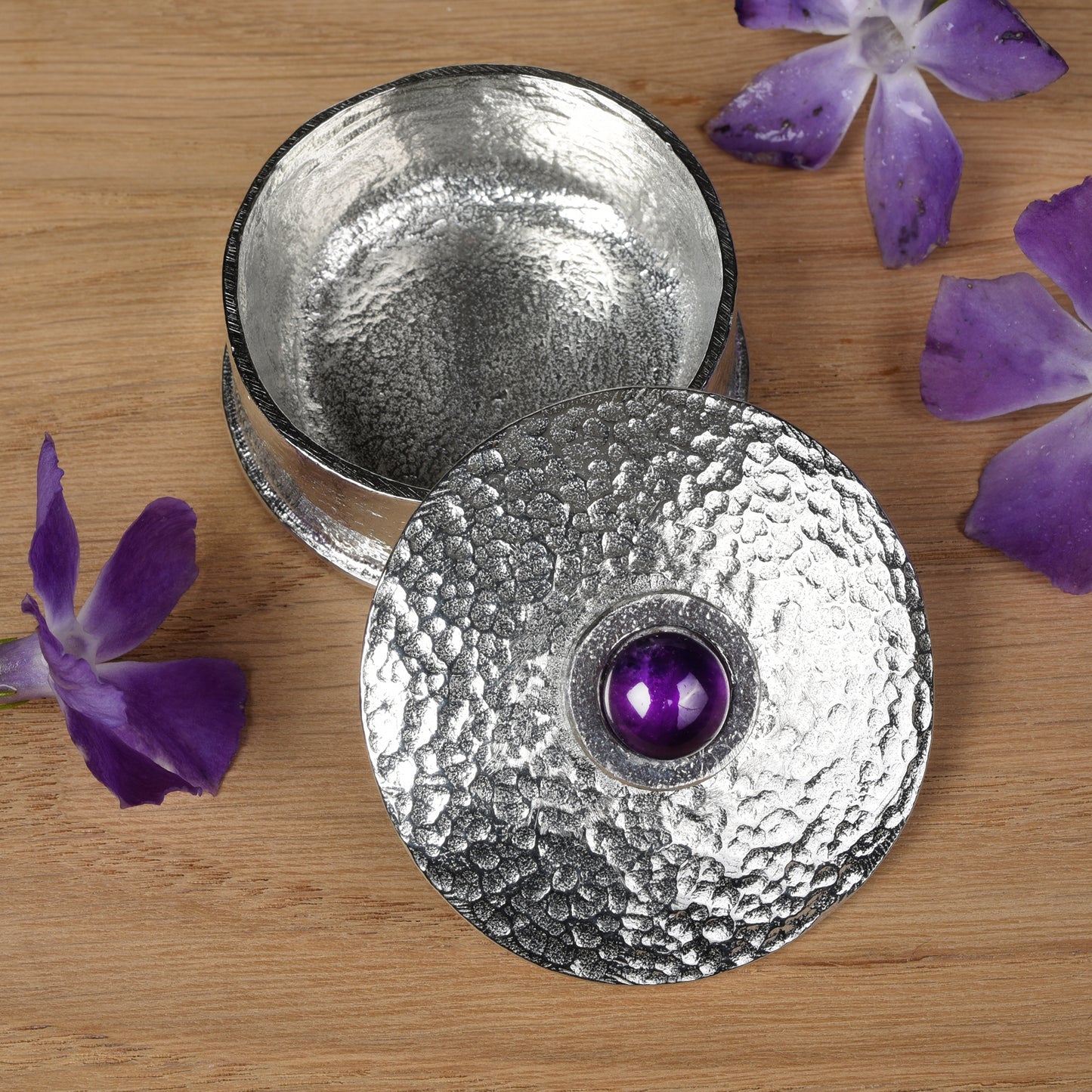 A simple textured pewter trinket box with a 10mm amethyst set into the centre of the lid. Amethyst is the birthstone for February.