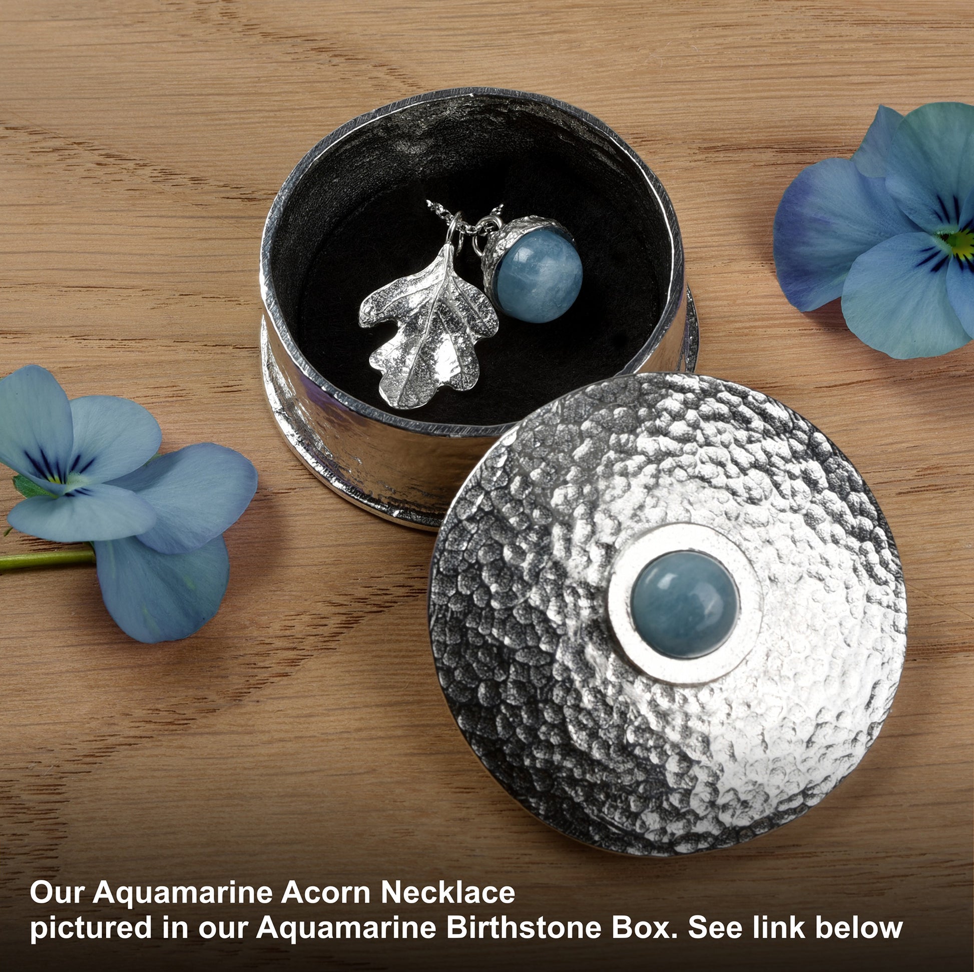 Aquamarine Acorn Necklace in an Aquamarine Birthstone Box with blue flowers on a wooden surface