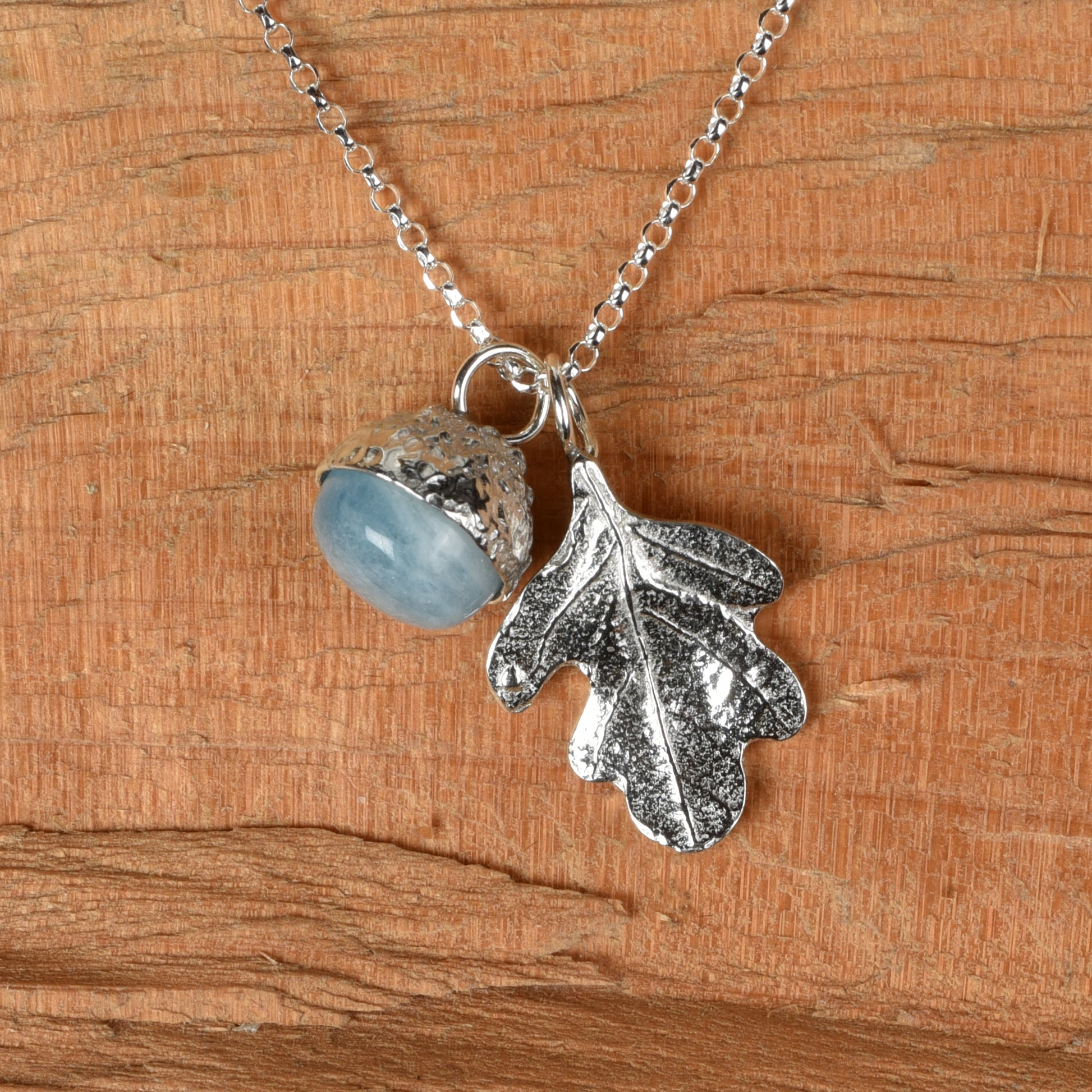 Pewter jewellery, an oak leaf necklace with an acorn cup with an aquamarine stone in it, March birthstone jewellery on a Sterling silver chain, natural wood background