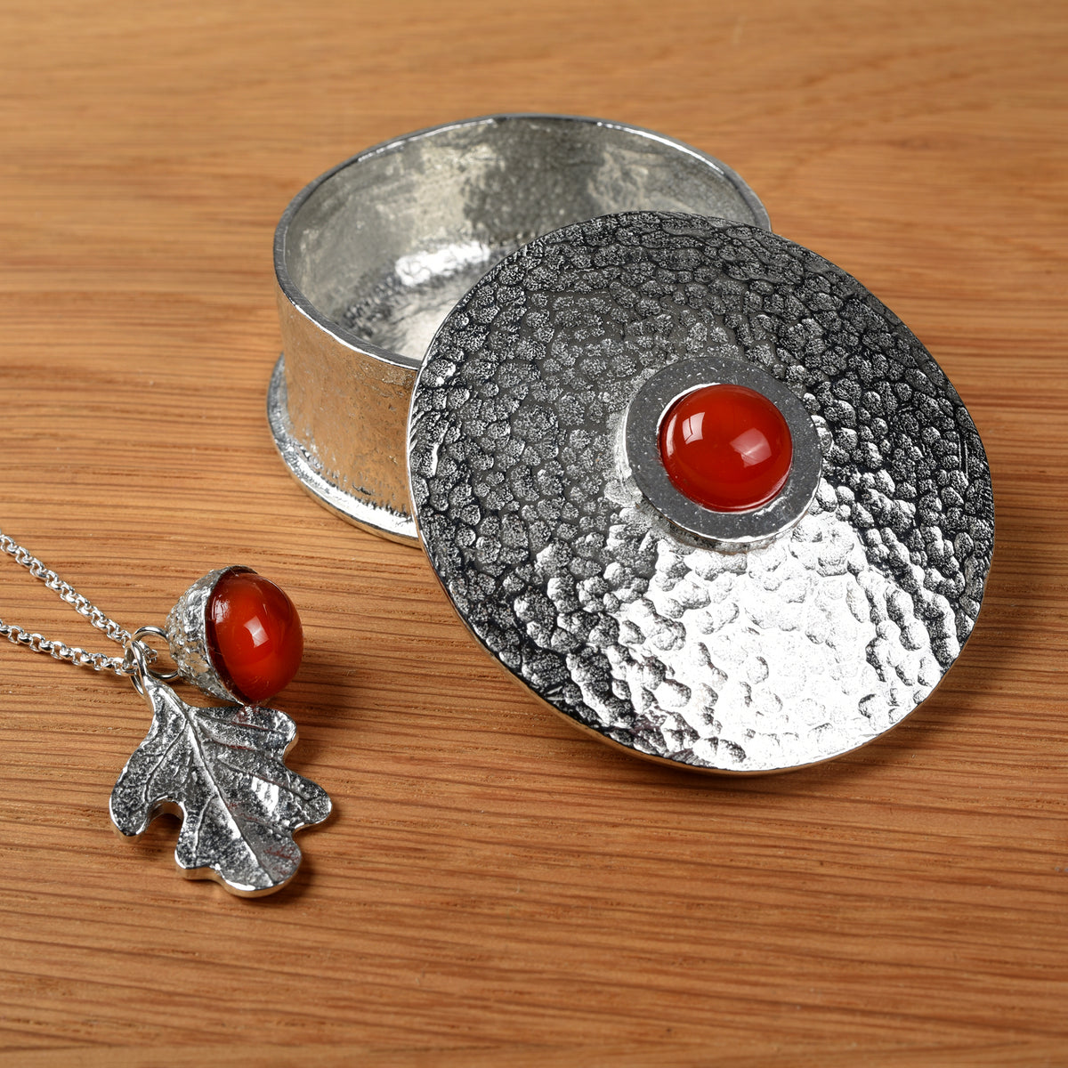 Carnelian engraved personalised pewter birthstone box with carnelian acorn and oak leaf necklace on a wooden surface