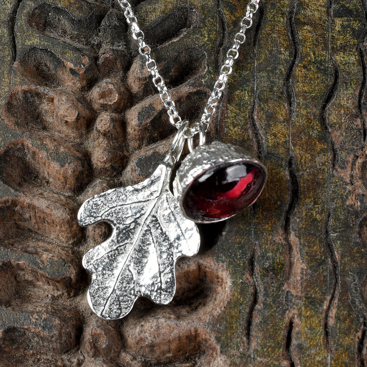 garnet acorn and oak leaf necklace on a textured wooden background