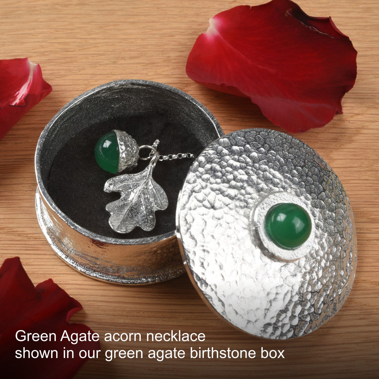 Green Agate acorn necklace in a pewter birthstone box with red rose petals on a wooden surface