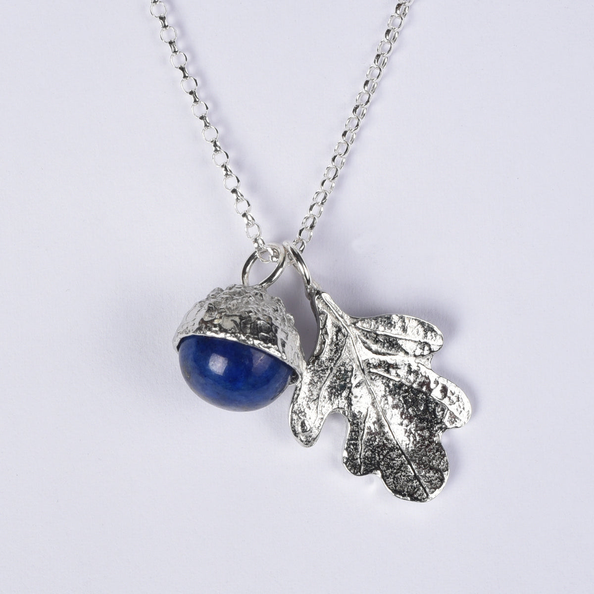 A pewter necklace with a dual pendant featuring a polished blue lapis lazuli stone acorn and a textured oak leaf, displayed on a white background.