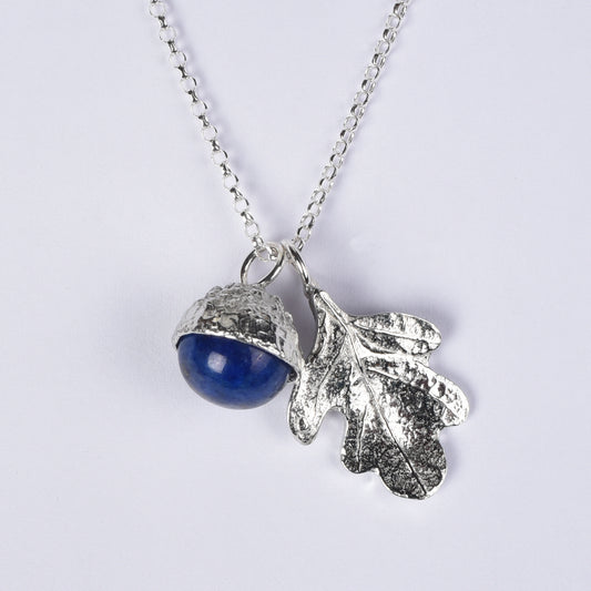 A pewter necklace with a dual pendant featuring a polished blue lapis lazuli stone acorn and a textured oak leaf, displayed on a white background.