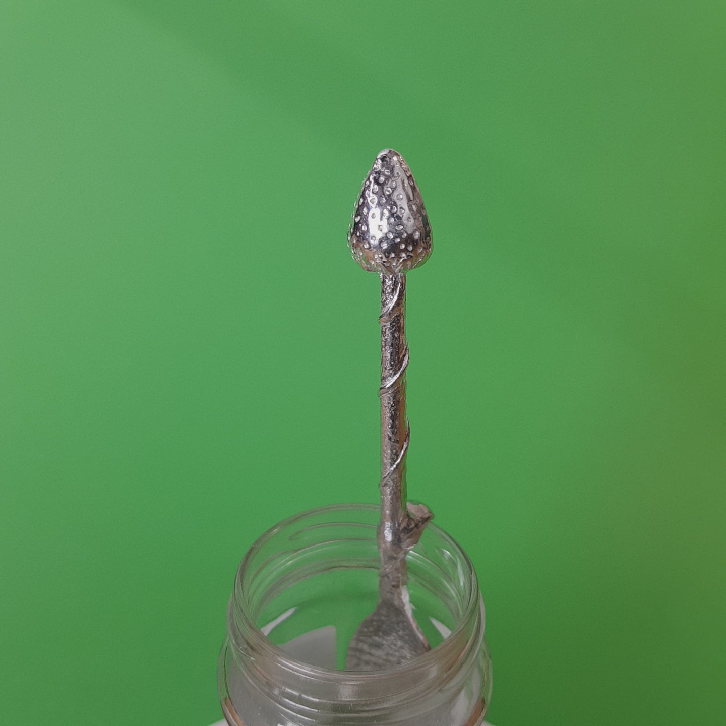 Long pewter jam spoon with a hook to hang on any jar. The top of the spoon has a strawberry sculpture on it.