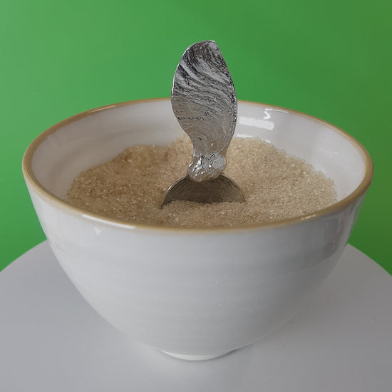 Video of a handmade pewter spoon with a sycamore key handle. The spoon is in a revolving sugar bowl.