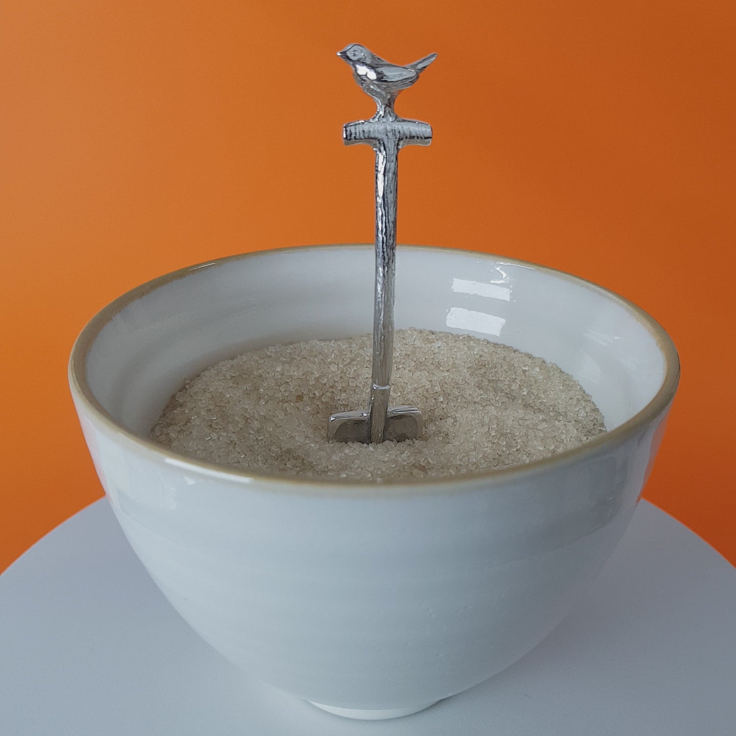 Video of a handmade pewter spoon in the shape of a garden spade. There is a robin on the handle. The spoon is in a revolving sugar bowl.