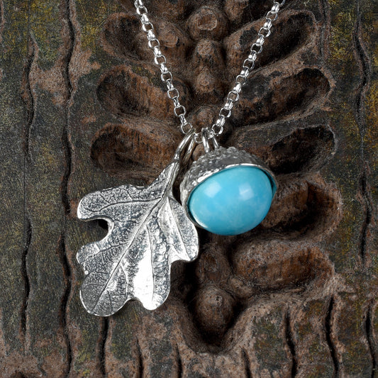 A  turquoise acorn and oak leaf pewter necklace. December birthstone gifts shown against a textured wooden background