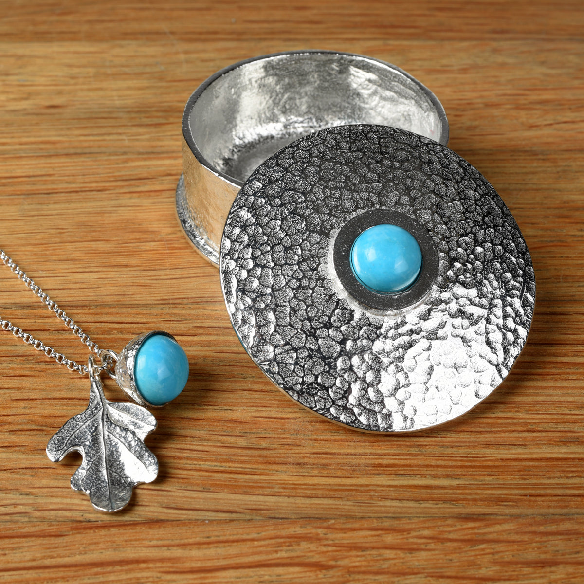 Round pewter box with a turquoise on the lid next to a turquoise acorn and oak leaf necklace. December birthstone gifts