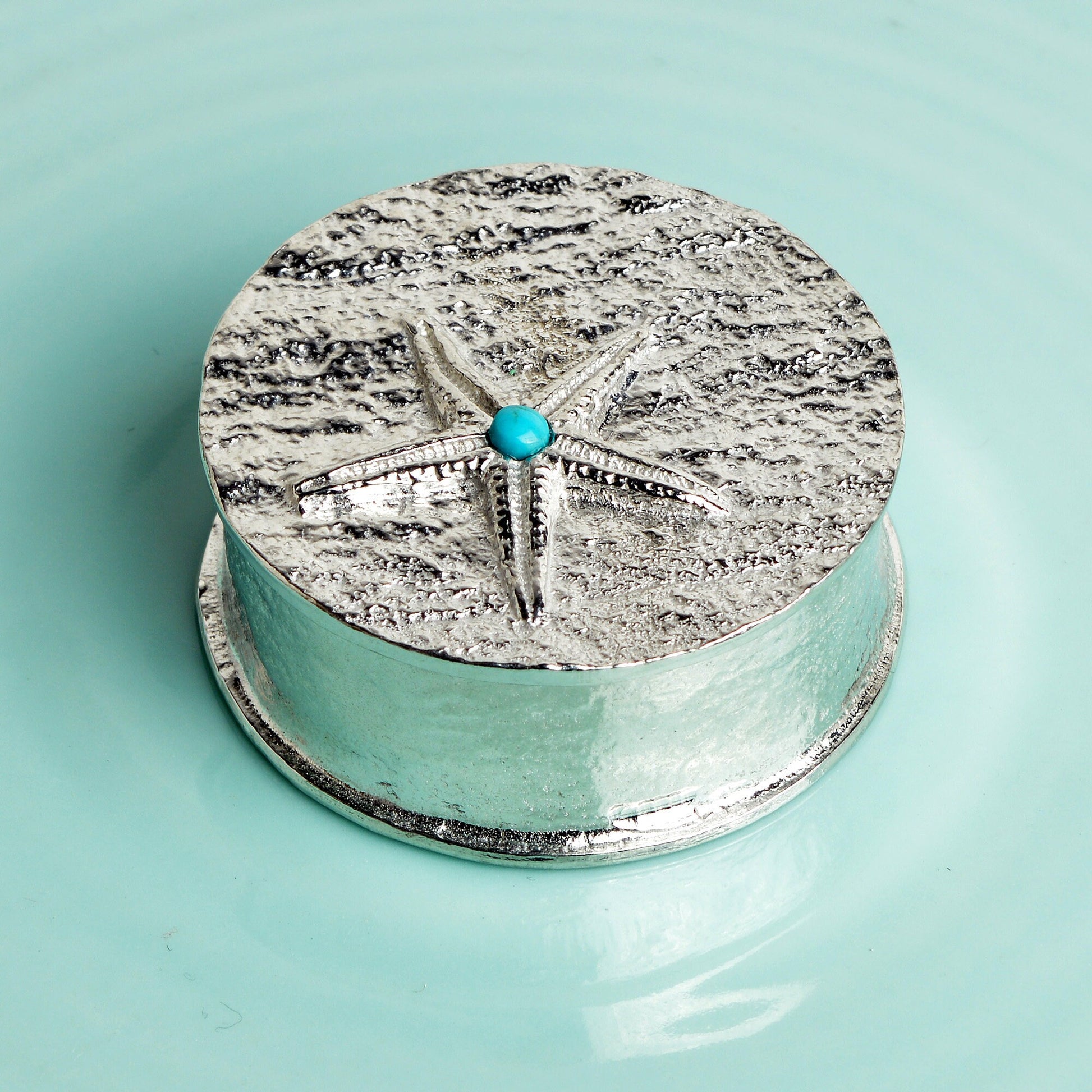 A round  pewter trinket box with a starfish on the lid. A turquoise stone sits on the meeting point of the 5 legs. Nautical gifts for lovers of the seaside and sea life.