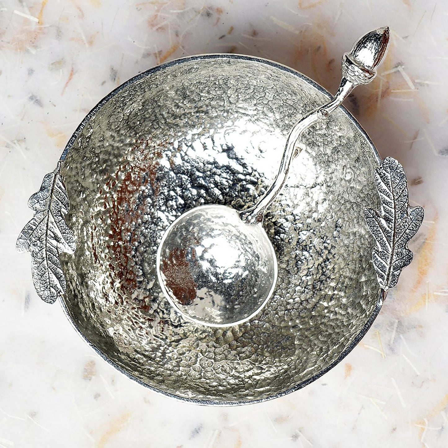 A 9cm diameter textured circular pewter bowl, with two oak leaves on the edge of the dish, comes with accompanying acorn spoon. Gifts for nature lovers, oak and acorn gifts. 'Great oaks from little acorns grow'.