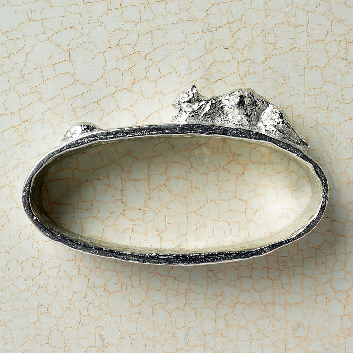 A set of 6 textured pewter oval-shaped napkin rings. Each one has a sculpture of an animal persuing its favourite food. A hedgehog and snail, a mouse and cheese, a frog and insect, a rabbit and carrot, a tortoise and leaf and a squirrel and acorn.